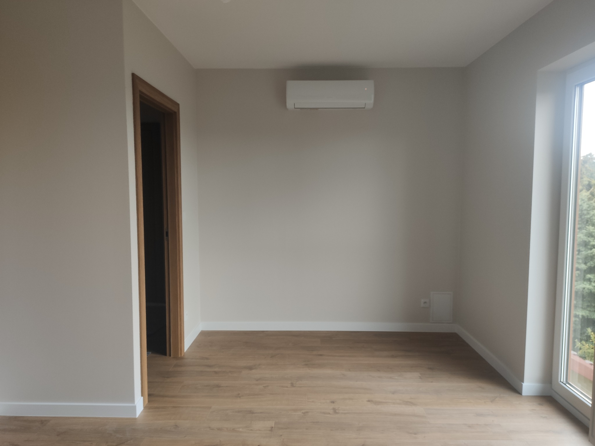 Jasne wnętrze po remoncie w Wieliczce: panele podłogowe w odcieniach drewna, białe listwy przypodłogowe, świeżo pomalowane ściany i zamontowany klimatyzator.