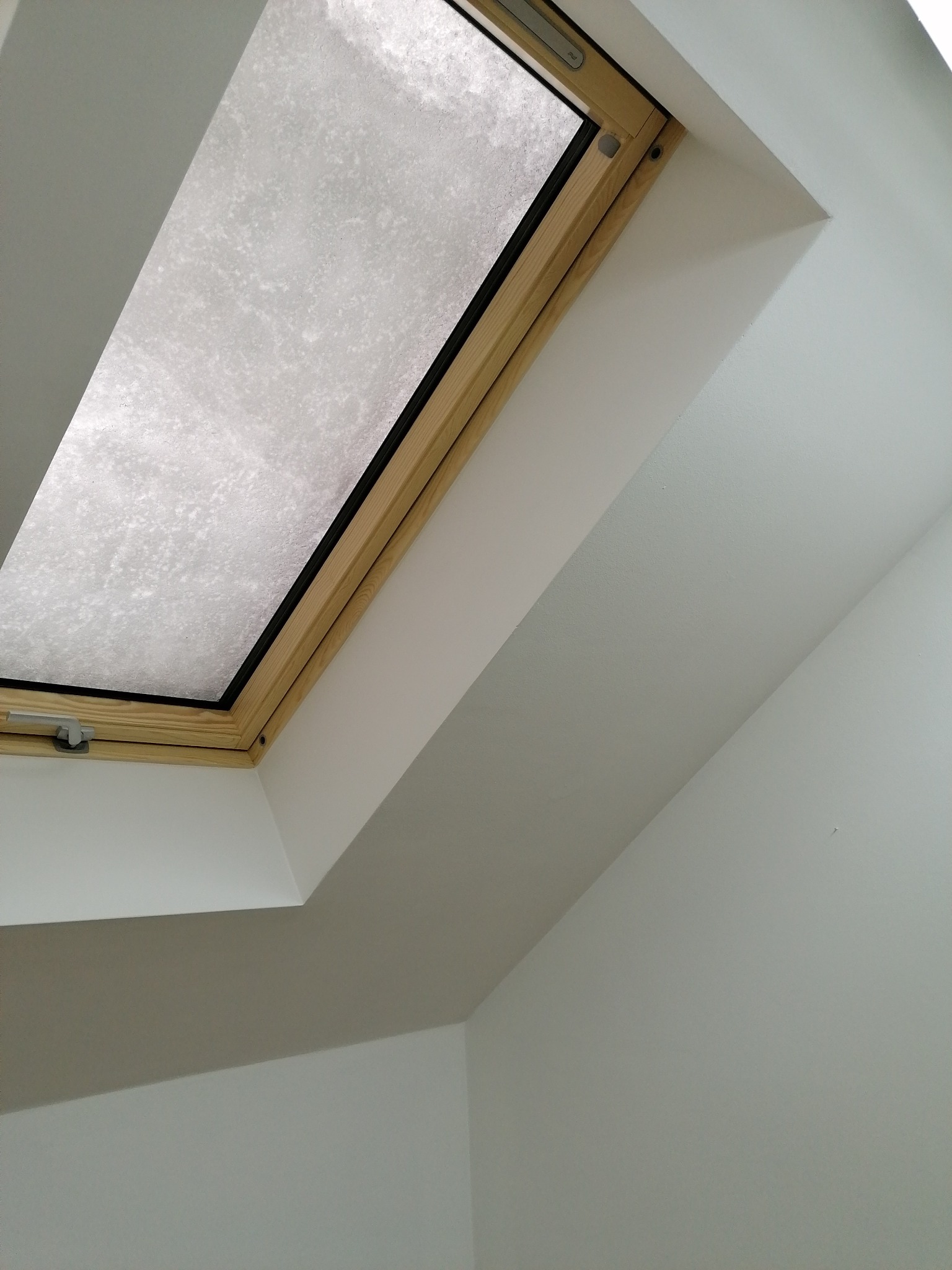 Zamontowane okno dachowe z drewnianą ramą w skosie poddasza, widoczne białe ściany i sufit.