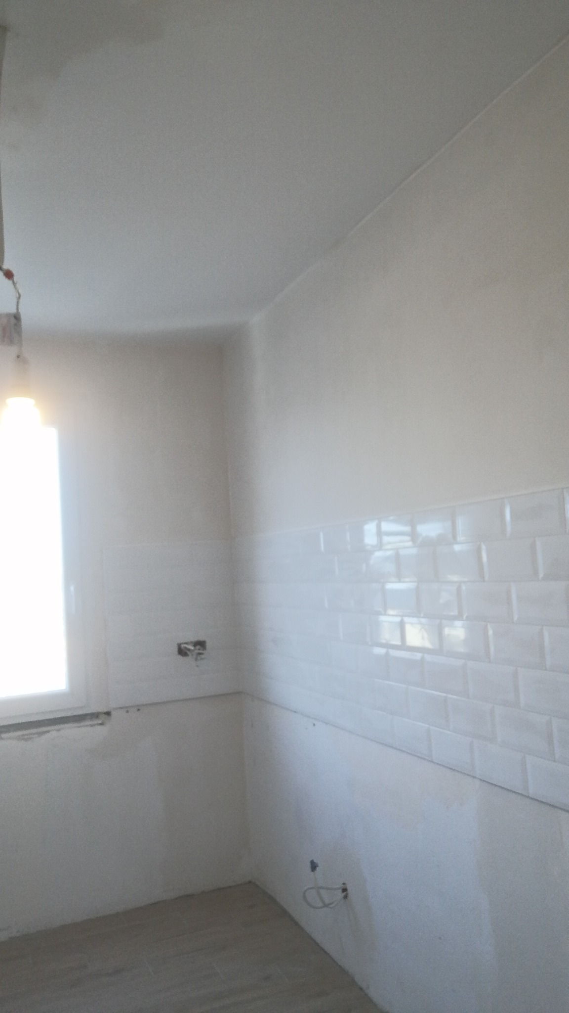 Wnętrze łazienki w trakcie prac wykończeniowych, widoczne białe płytki typu metro na ścianie, świeżo pomalowany sufit i ściany, oraz podłoga wyłożona panelami imitującymi drewno.