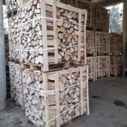 Ułożone w skrzyniach i zabezpieczone taśmą pocięte kawałki drewna, gotowe do transportu i spalenia w kominku, widoczne drewniane palety.