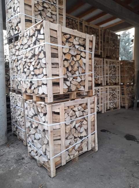 Ułożone w skrzyniach i zabezpieczone taśmą pocięte kawałki drewna, gotowe do transportu i spalenia w kominku, widoczne drewniane palety.