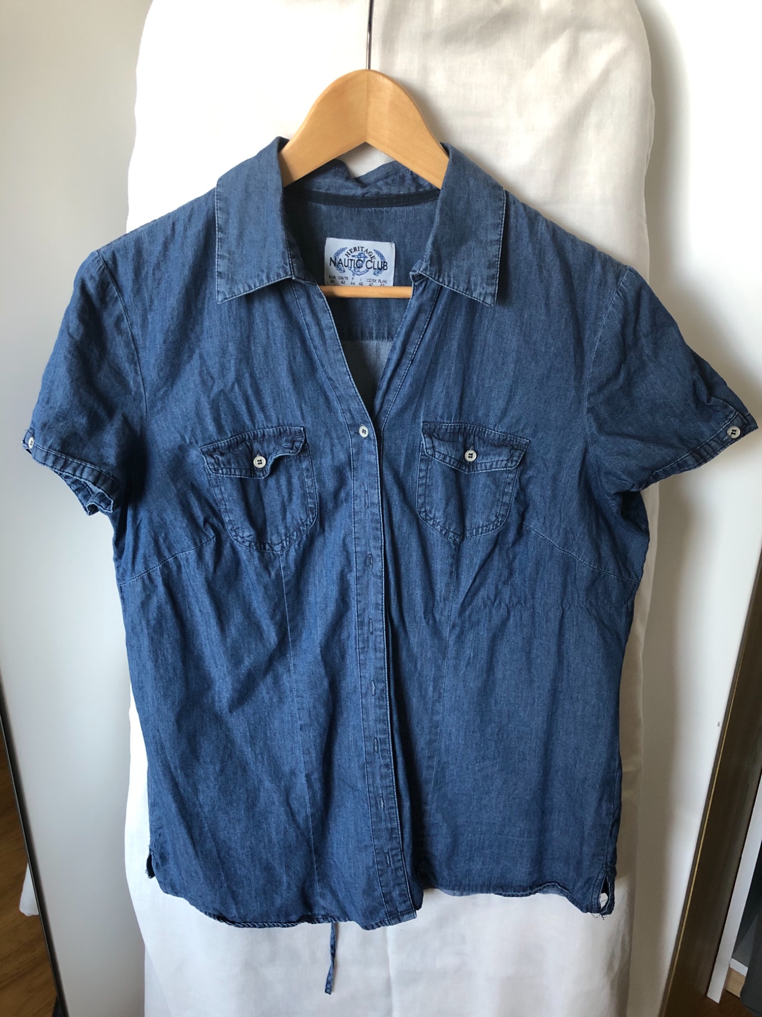 Koszula damska z denimu marki Nautica Club, wisząca na drewnianym wieszaku na tle białej tkaniny.