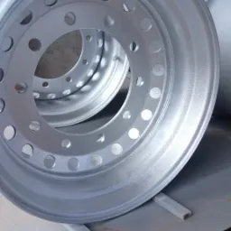 Dwa srebrne felgi samochodowe z otworami na śruby, świeżo po malowaniu proszkowym, ustawione na metalowej powierzchni w warsztacie.