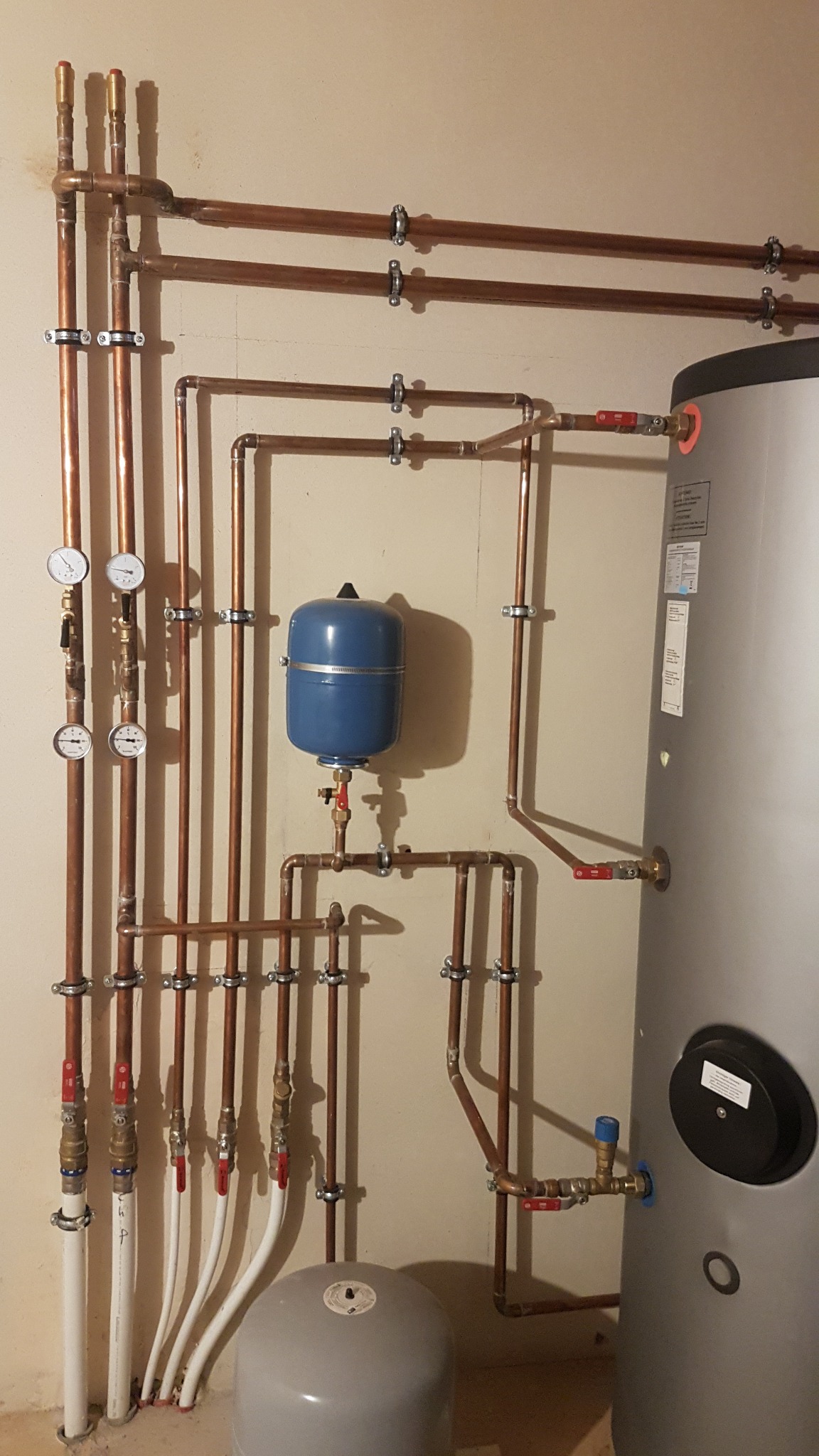 Instalacja grzewcza z miedzianymi rurami, manometrami i zbiornikami wyrównawczymi w kotłowni, wykonana przez firmę z Poznania.