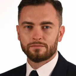 Portret mężczyzny z brodą w garniturze i krawacie na białym tle.