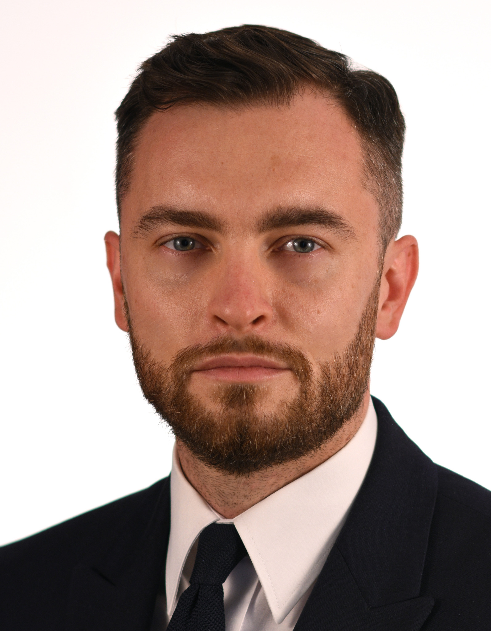 Portret mężczyzny z brodą w garniturze i krawacie na białym tle.