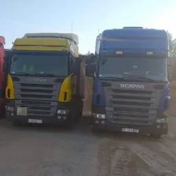 Dwa samochody ciężarowe marki Scania, żółty i niebieski, stoją na piaszczystym terenie. Widoczne numery rejestracyjne BI-660CX i BI-510EF. Ujęcie z dołu, na tle błękitnego nieba.