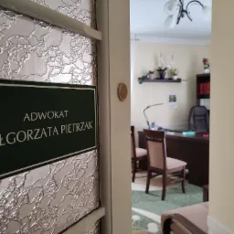 Tabliczka z napisem 'Adwokat Małgorzata Pietrzak' na drzwiach z dekoracyjnym szkłem, widok na wnętrze kancelarii z biurkiem i krzesłami.