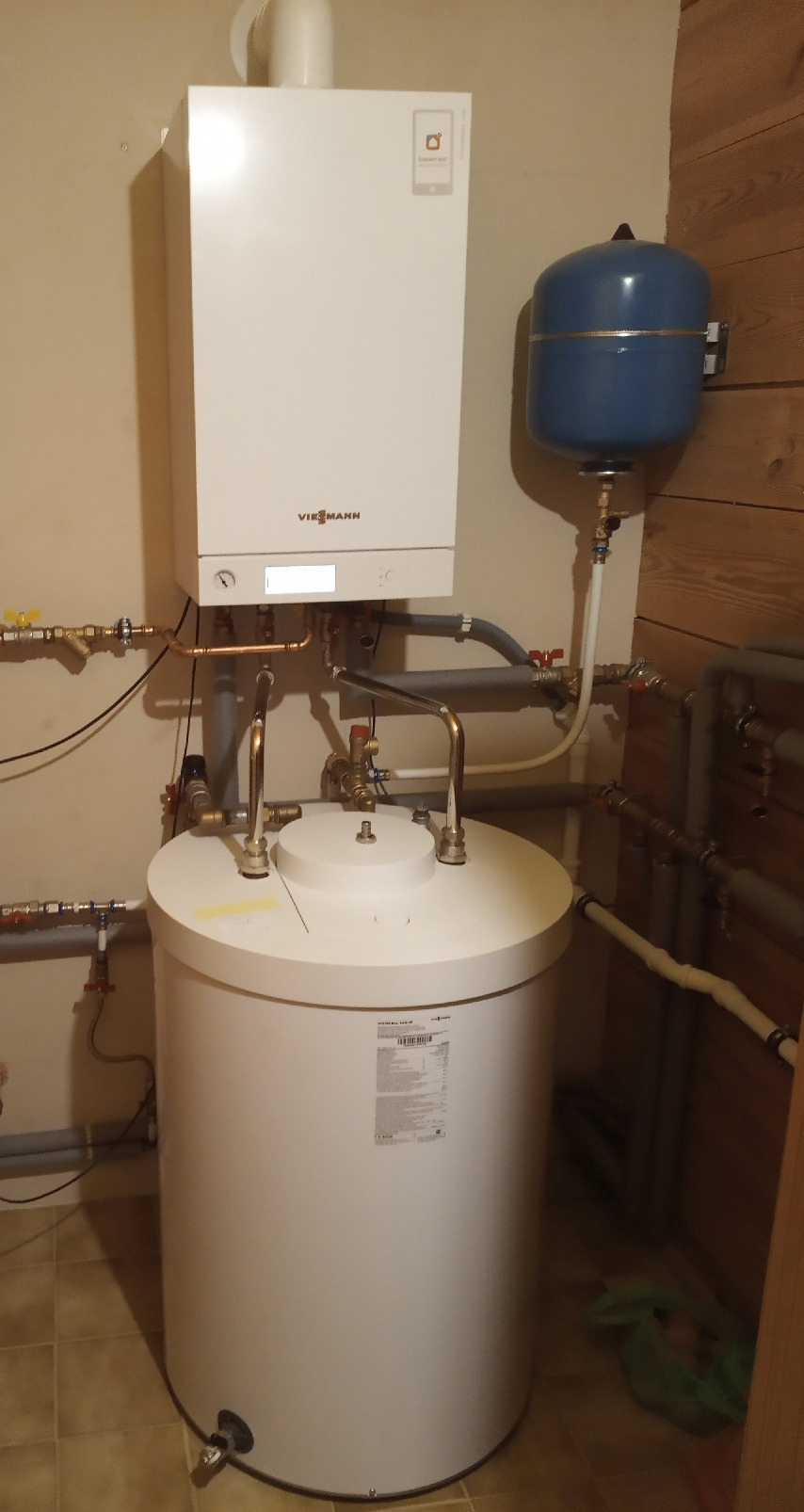 Kocioł grzewczy Viessmann z zasobnikiem ciepłej wody i niebieskim naczyniem przeponowym, zamontowany przy ścianie z boazerią.