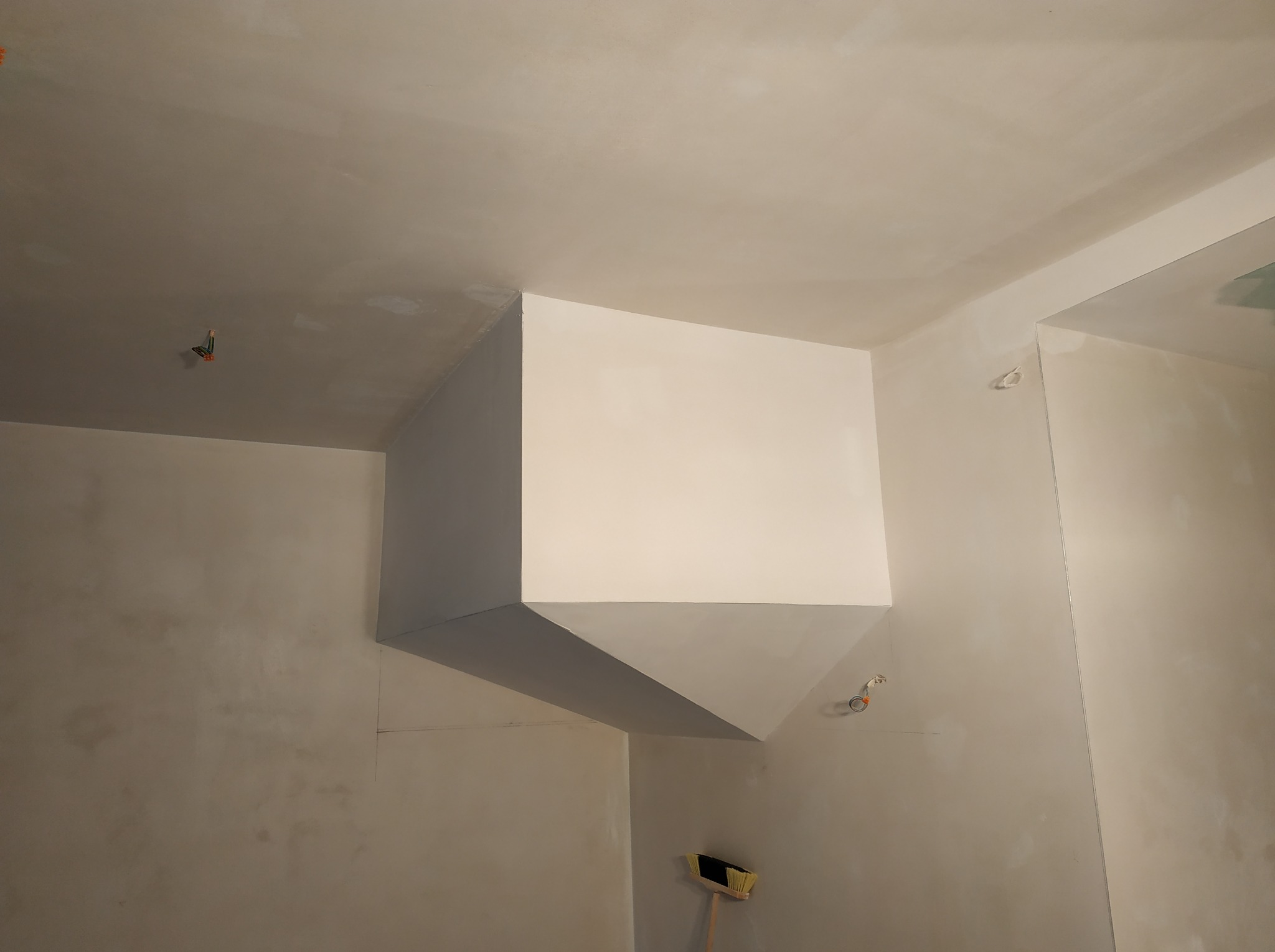 Narożnik sufitu z nałożoną białą gładzią, widoczne ślady szpachlowania na ścianach i suficie, przygotowanie do malowania, w rogu pomieszczenia stoi miotła.