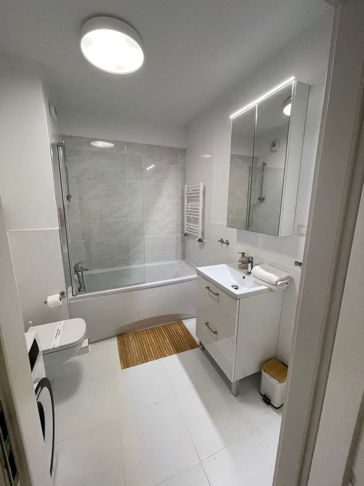 Jasna łazienka we Wrocławiu po sprzątaniu: białe płytki, wanna z parawanem, umywalka z szafką, bambusowy dywanik i akcesoria. Czystość i minimalizm.