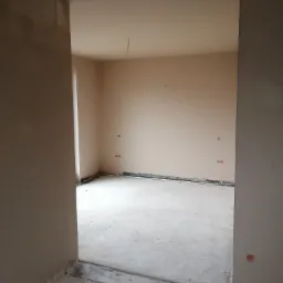 Pokój po nałożeniu gładzi gipsowej, widoczne przygotowane ściany i podłoga przed malowaniem, instalacja elektryczna częściowo wyprowadzona.