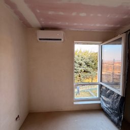 LDR Electrical Dariusz Karaś - Klimatyzator ścienny zamontowany w surowym wnętrzu w Jaśle. Widoczne przygotowania do wykończenia ścian i sufitu. Otwarta okno z widokiem na zewnątrz.