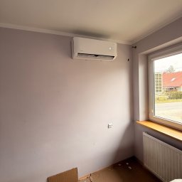 LDR Electrical Dariusz Karaś - Biały klimatyzator ścienny Intenso zamontowany w pokoju z fioletowymi ścianami, widok na okno i grzejnik. Podłoga zabezpieczona kartonem.