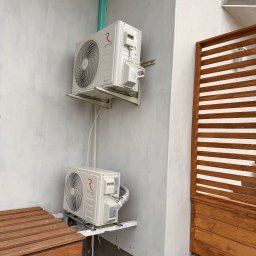 LDR Electrical - Dwa klimatyzatory Rotenso zamontowane na szarej ścianie budynku, widoczne elementy instalacji i drewniana konstrukcja w tle. Ujęcie z dołu.