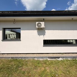 LDR Electrical - Biała elewacja domu z zamontowaną jednostką zewnętrzną klimatyzacji, widoczne okna i trawnik. Błękitne niebo z chmurami w tle.