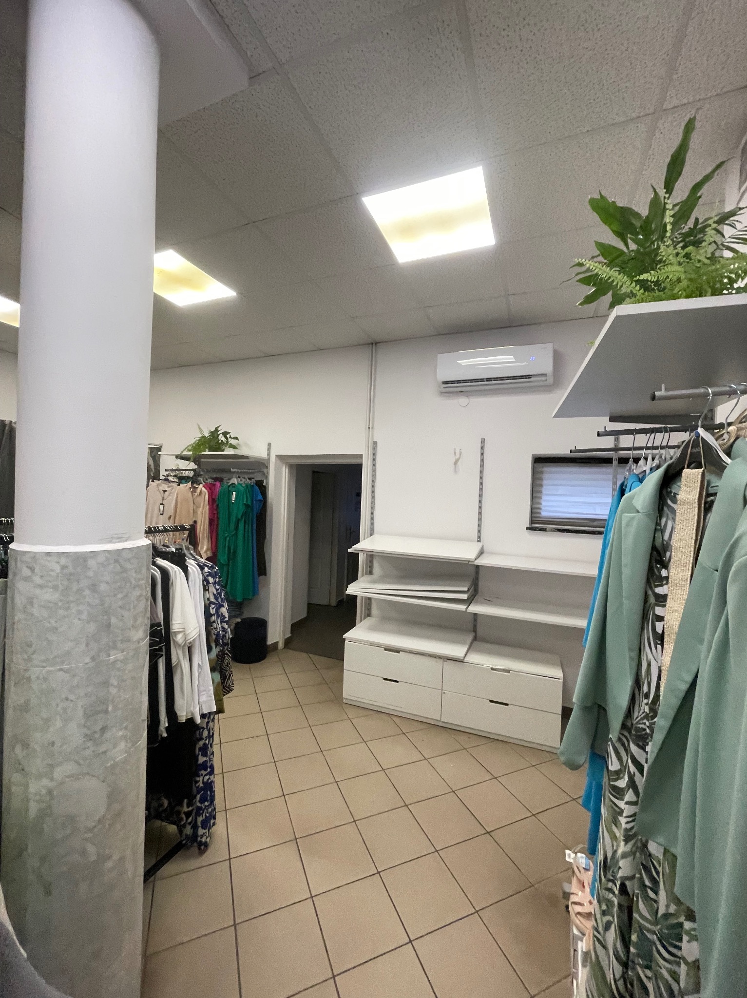 Wnętrze sklepu odzieżowego z zainstalowaną klimatyzacją ścienną, widoczne w tle. Ubrania wiszą na wieszakach, a w pomieszczeniu znajduje się duży, dekoracyjny filar.