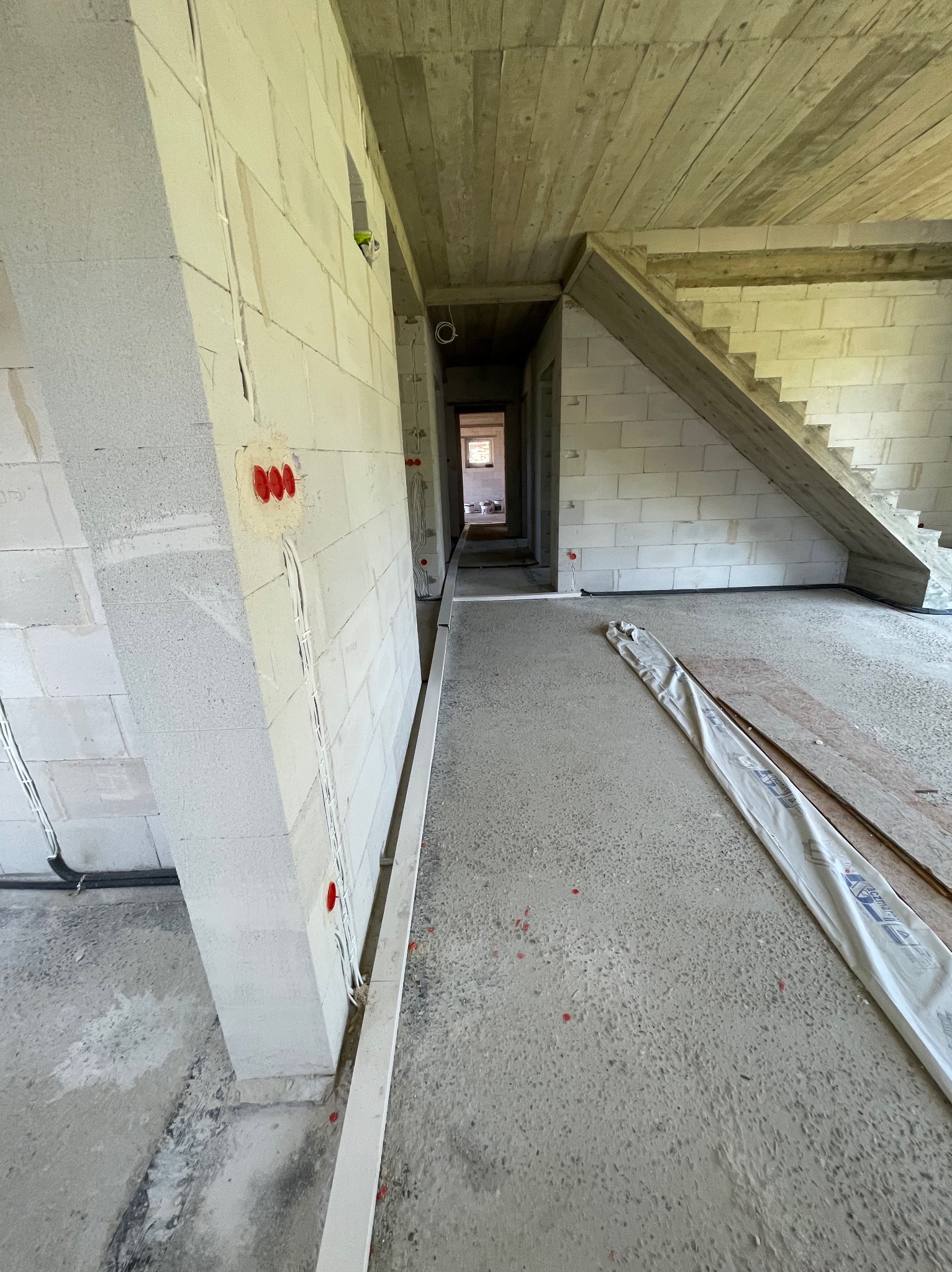 Wnętrze w stanie surowym: ściany z betonu komórkowego, widoczne przewody elektryczne w ścianach, surowy betonowy strop, schody w trakcie budowy.