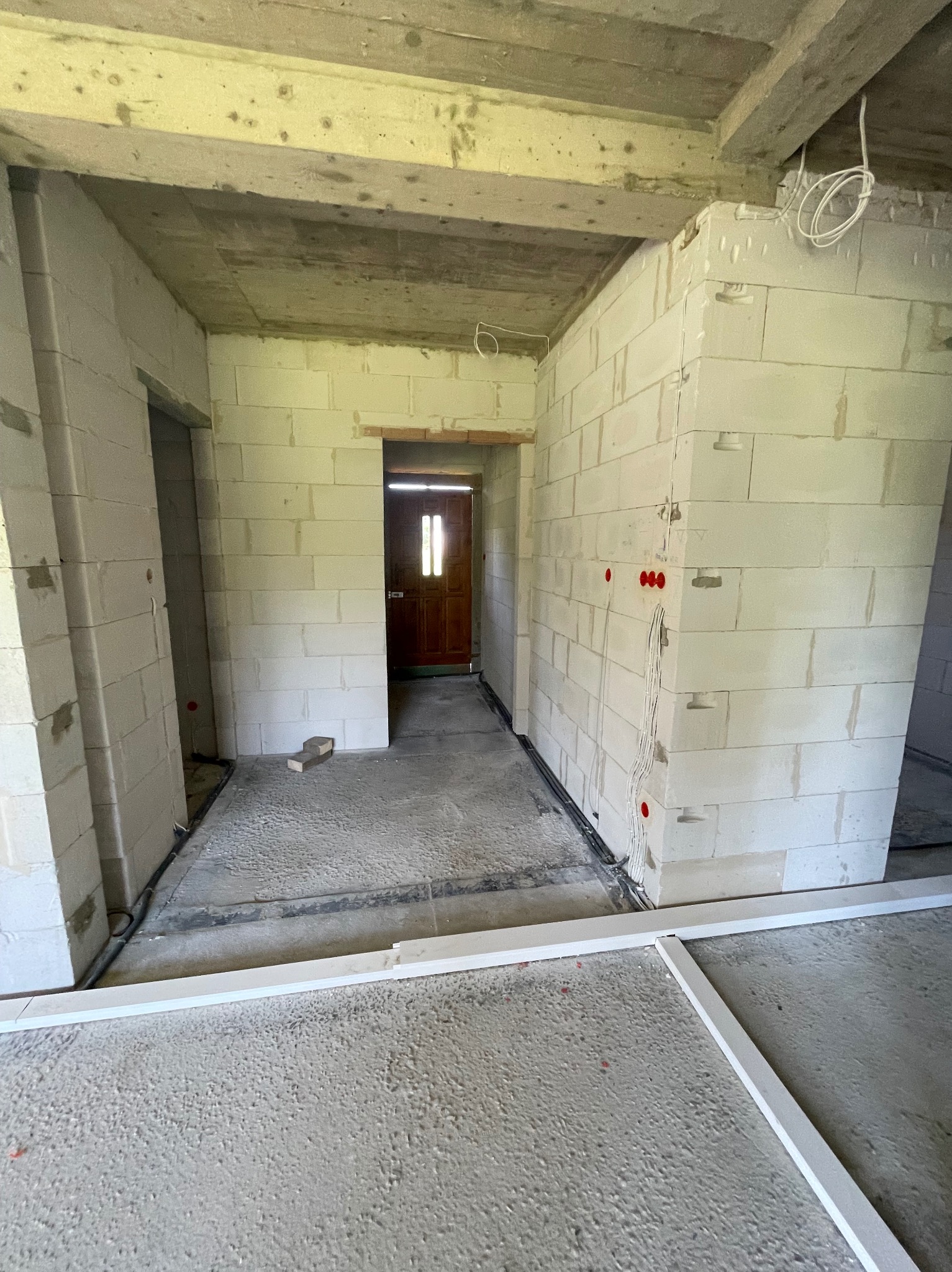 Wnętrze w stanie surowym z widocznymi instalacjami elektrycznymi w ścianach z betonu komórkowego. Na podłodze widoczne listwy przypodłogowe.