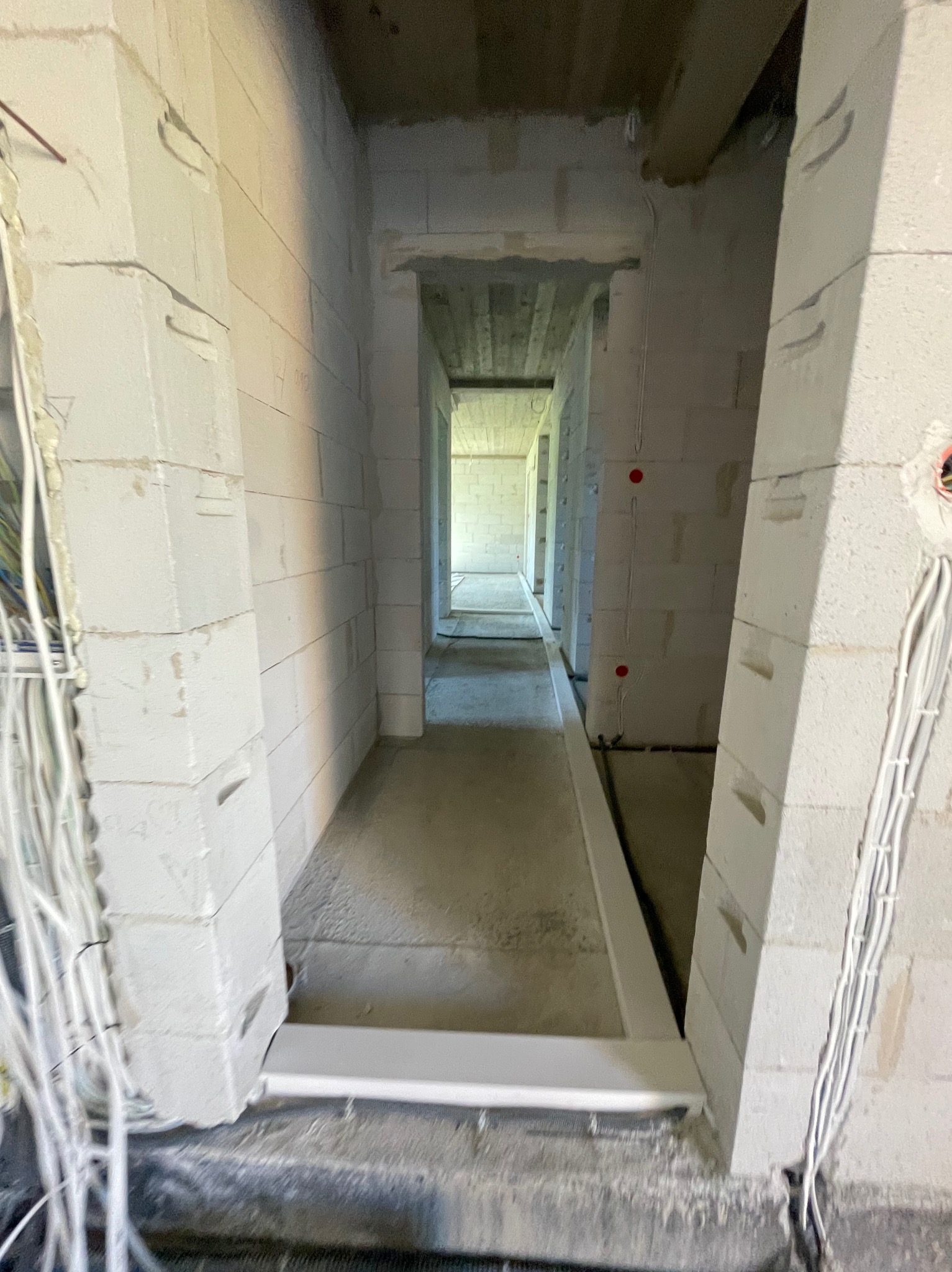 Surowy stan budynku w trakcie instalacji elektrycznej: widoczne przewody w ścianach z betonu komórkowego i puszki instalacyjne. Długi korytarz w perspektywie.