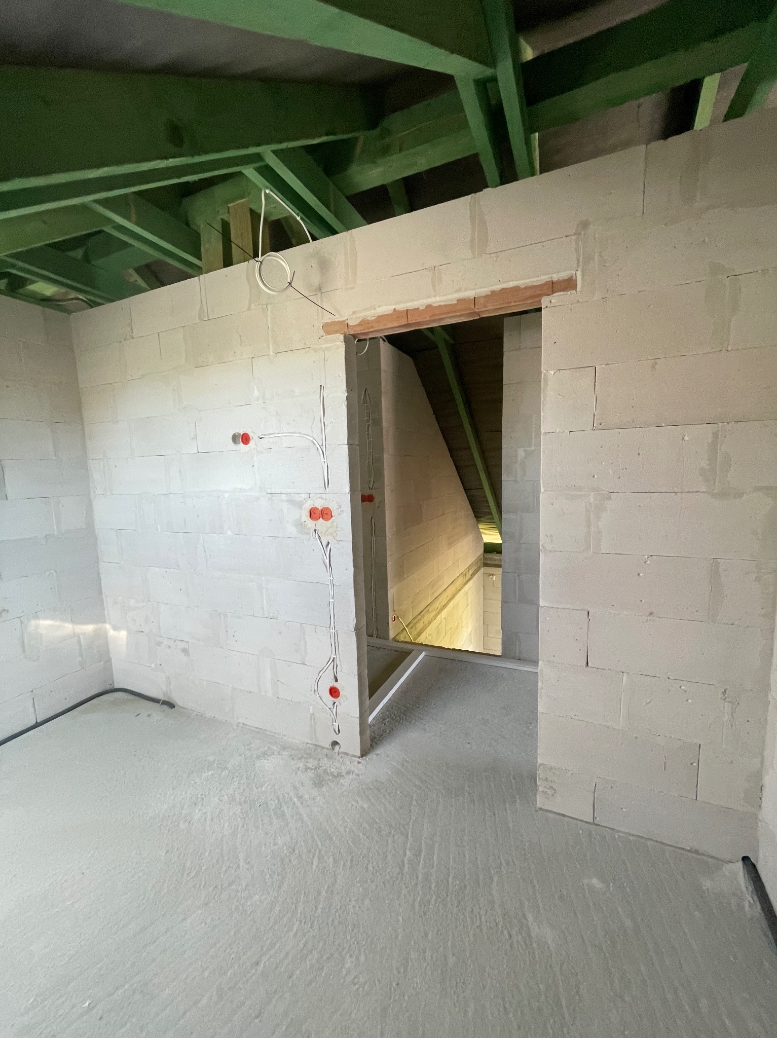 Surowy stan: wnętrze w trakcie instalacji elektrycznej, widoczne kable i puszki w ścianach z betonu komórkowego, zielona konstrukcja dachu.