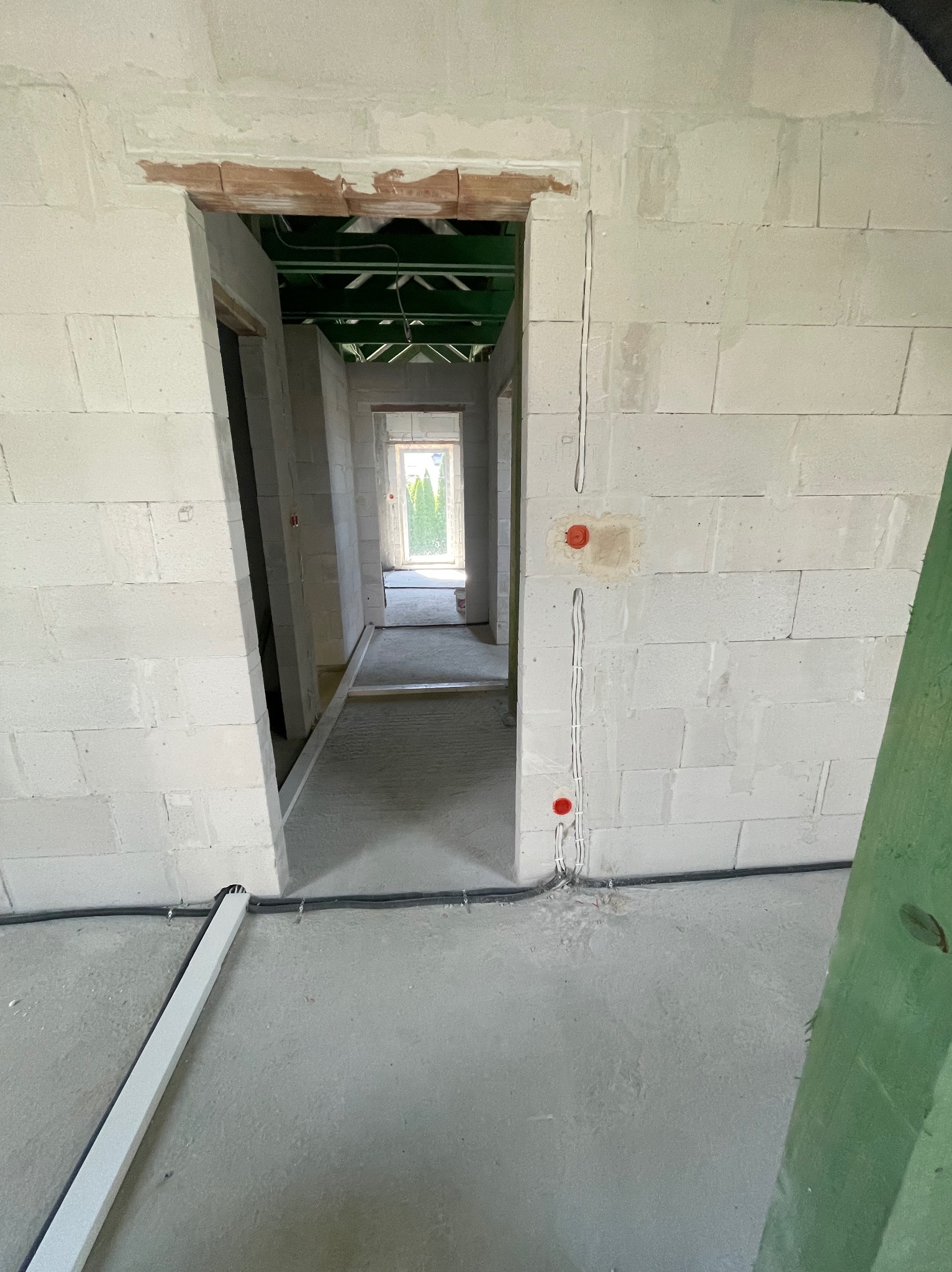 Wnętrze budynku w trakcie instalacji elektrycznej: widoczne kable w ścianach i pod sufitem, puszki elektryczne oraz przewody prowadzone wzdłuż podłogi. Surowy stan wykończenia.