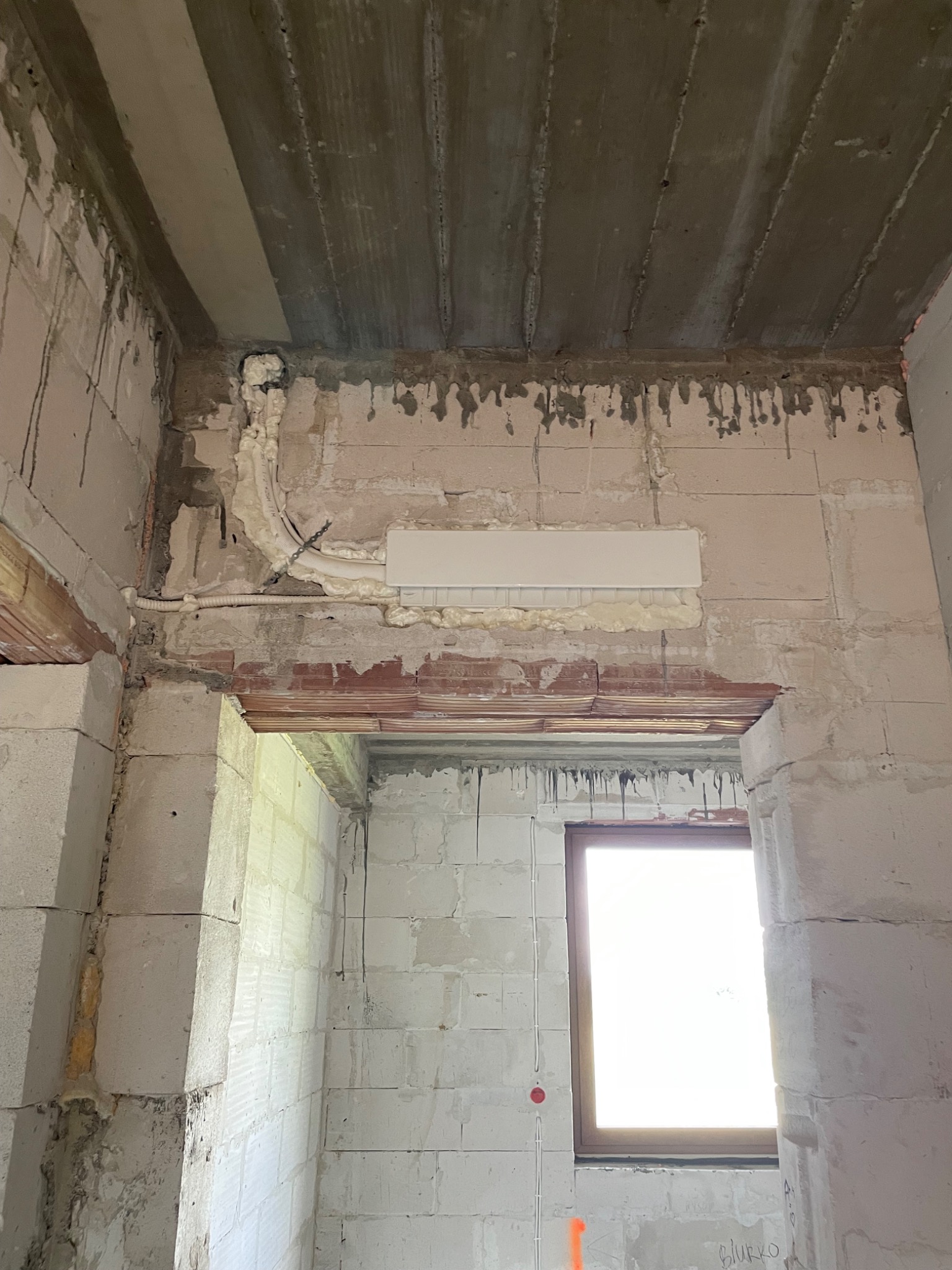 Wnętrze w stanie surowym: instalacja elektryczna w peszlu, zabezpieczona pianką montażową, widoczne przewody i puszka. Ściany z betonu komórkowego, surowy strop.