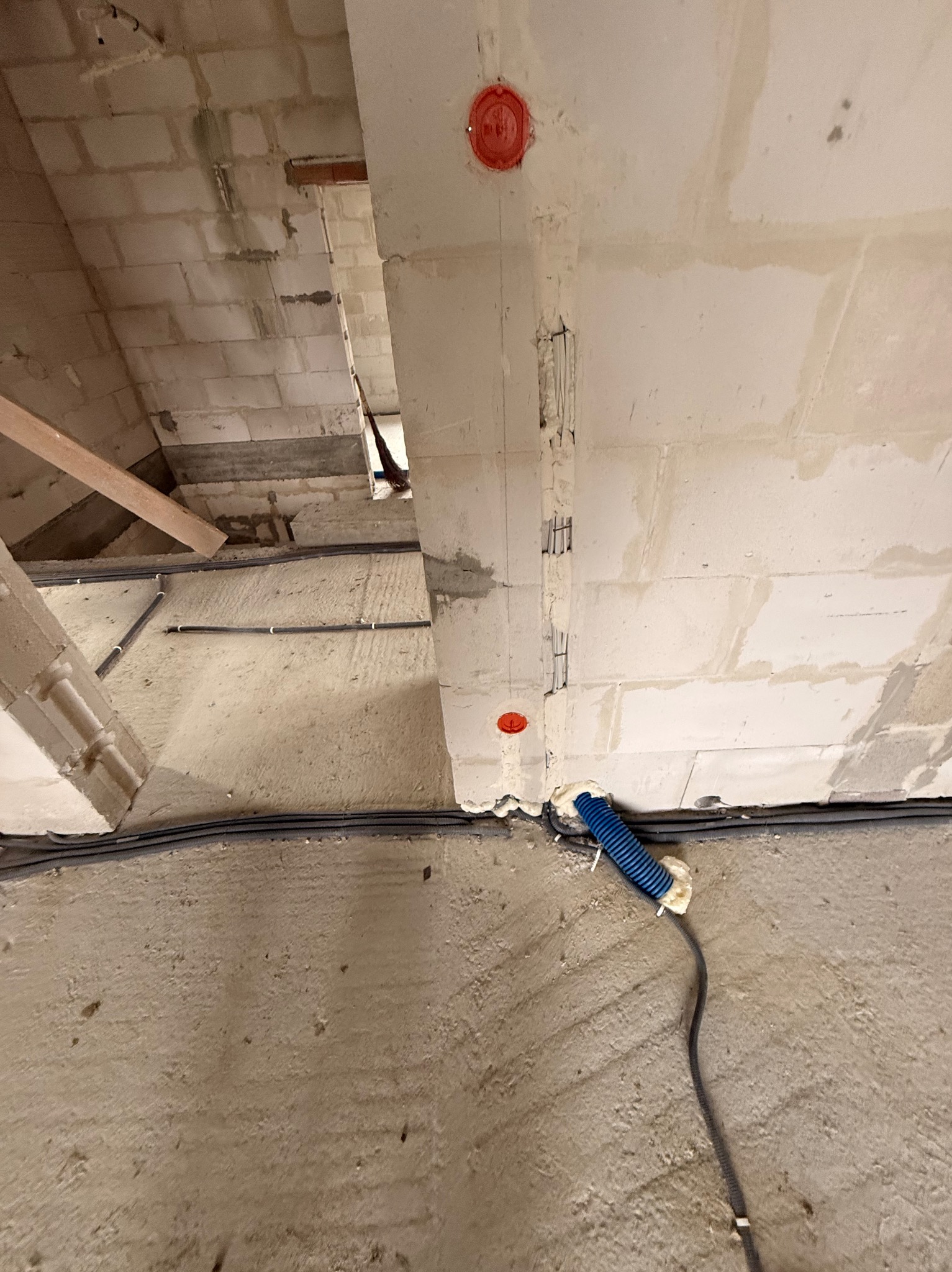 Szare kable elektryczne ułożone wzdłuż surowej ściany z betonu komórkowego, z widoczną puszką instalacyjną i niebieską rurką karbowaną, w trakcie prac instalacyjnych.