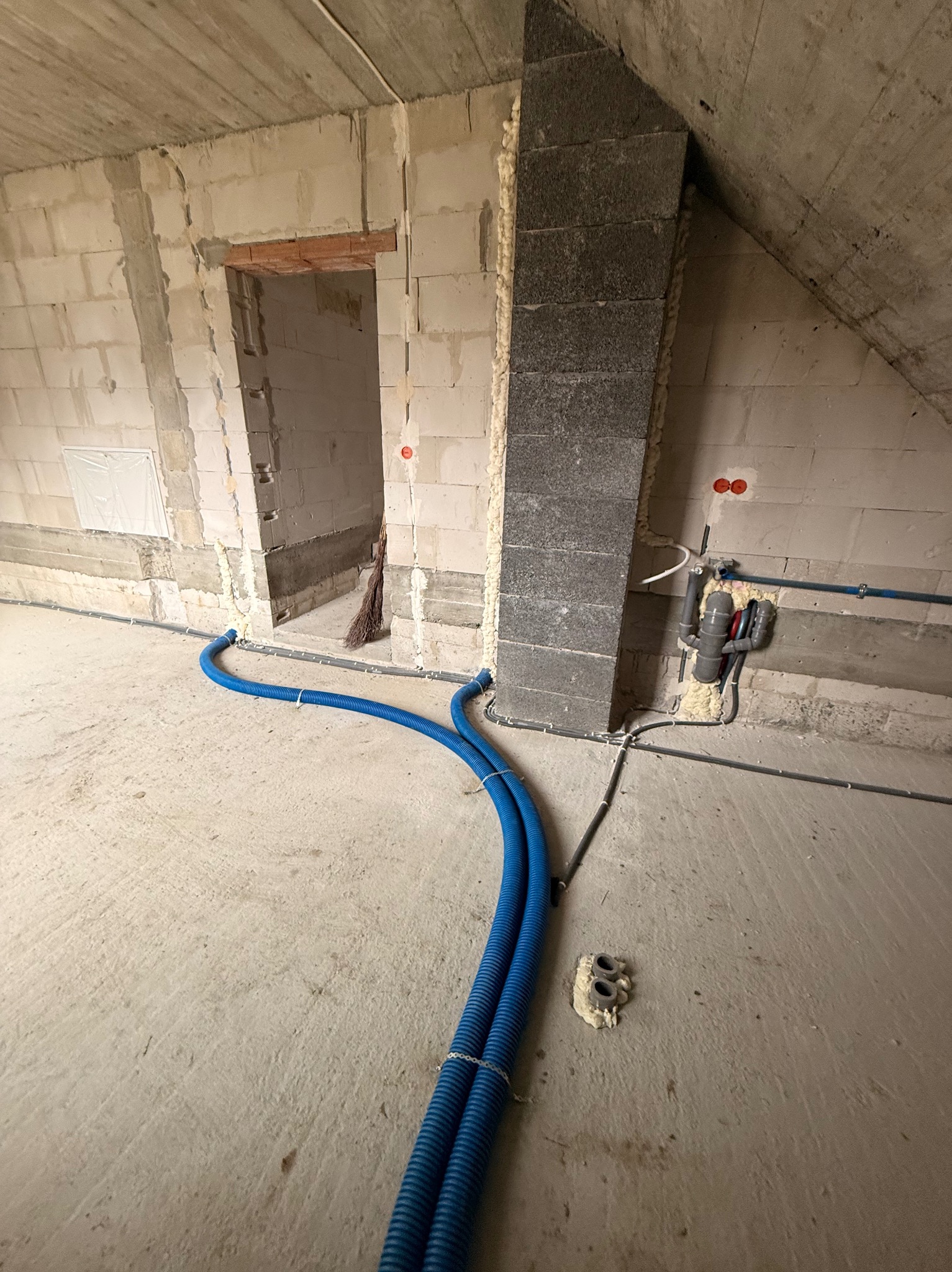 Niebieskie rury instalacyjne w surowym wnętrzu w Jaśle. Widoczne przewody i elementy montażowe. Ściany z pustaków, surowy beton. Instalacja w trakcie realizacji.