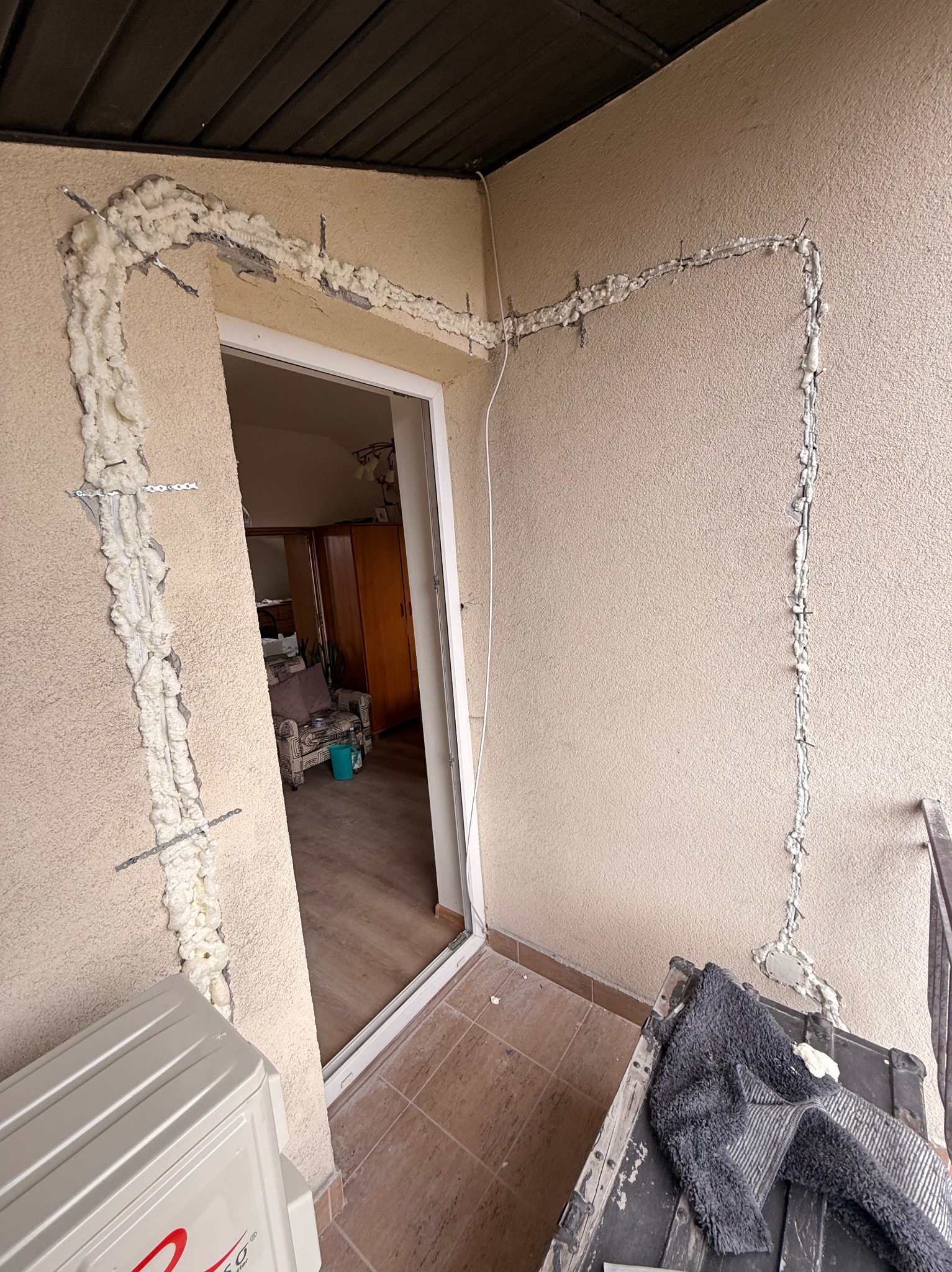 Montaż klimatyzacji na balkonie: bruzdy w ścianie wypełnione pianką montażową, widoczne przewody i fragment klimatyzatora. Etap prac instalacyjnych.