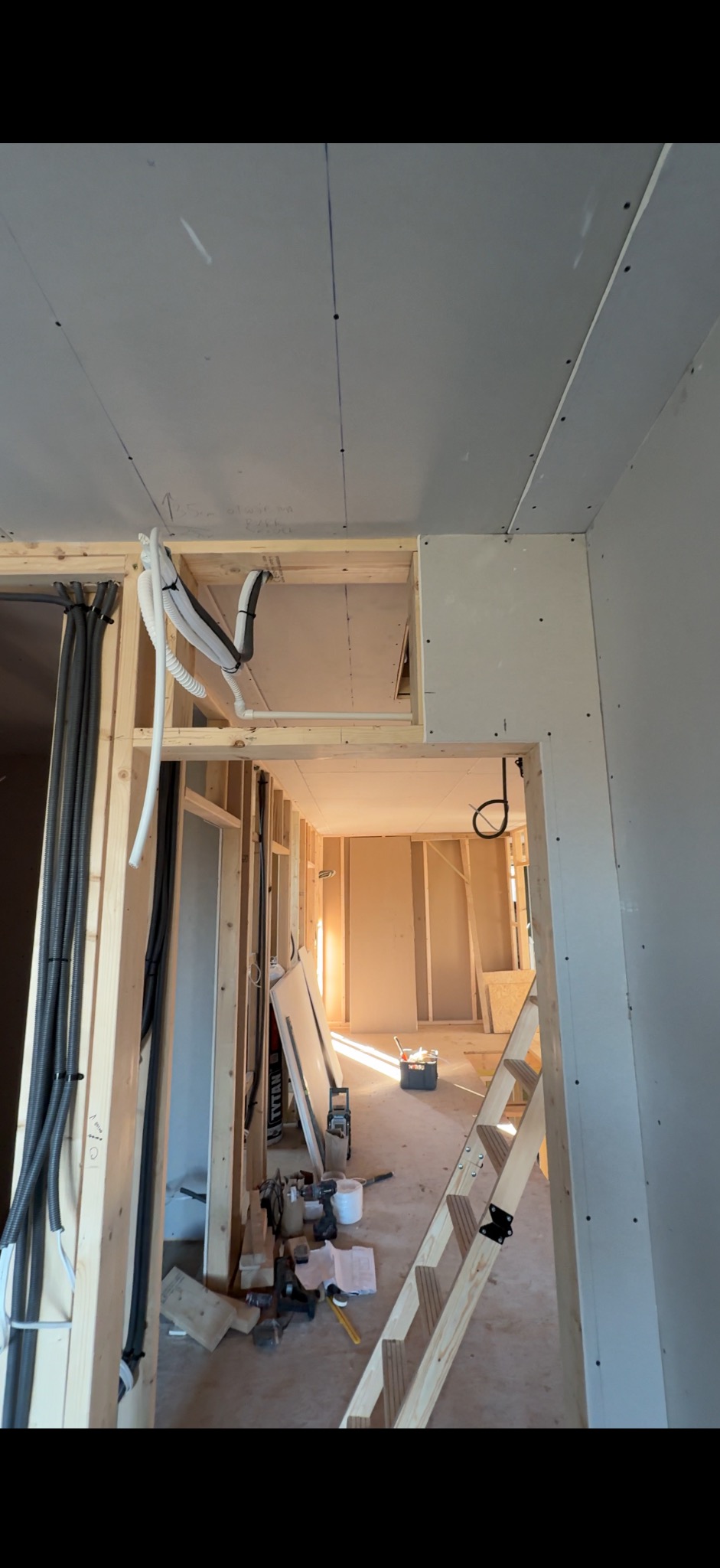 Wnętrze w trakcie prac instalacyjnych: widoczne kable elektryczne w peszlach, drewniana konstrukcja ścian działowych i sufit podwieszany z płyt gipsowo-kartonowych.