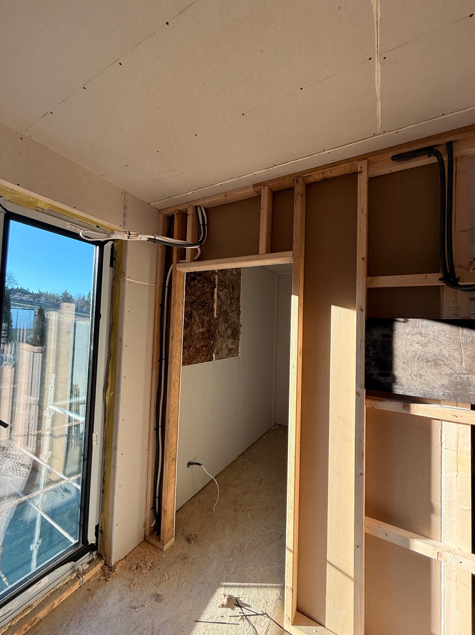 Wnętrze w trakcie prac wykończeniowych: widoczne drewniane ramy ścian działowych, instalacje elektryczne w peszlach i częściowo zamontowane płyty gipsowo-kartonowe.