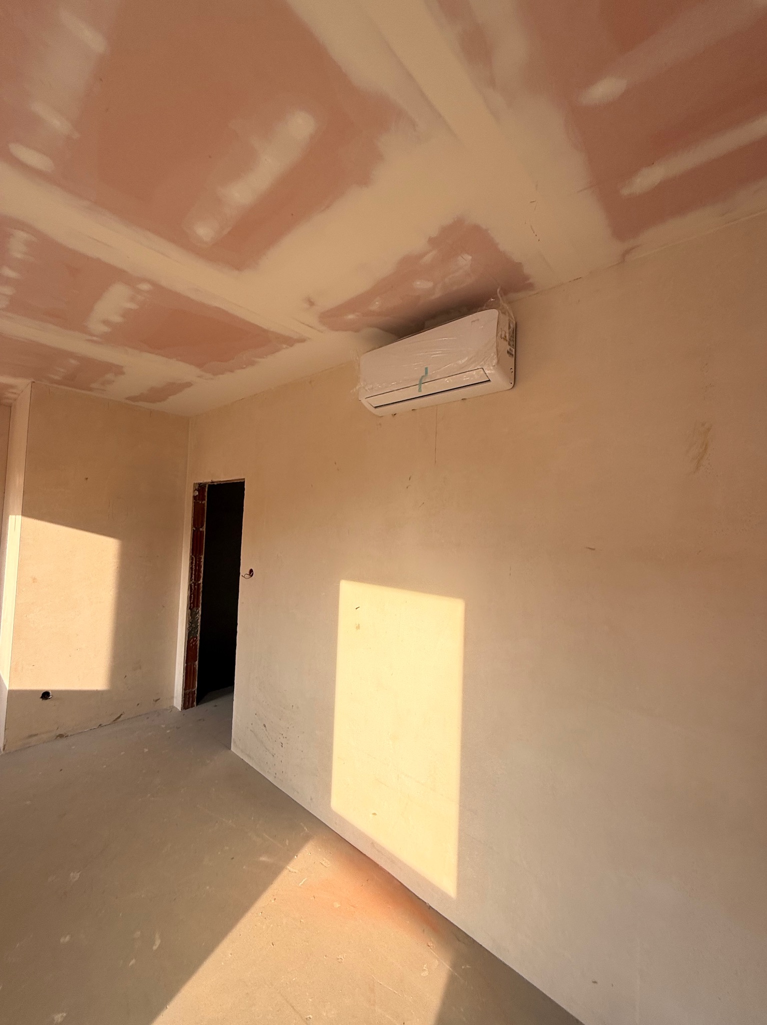 Wnętrze w trakcie remontu z zamontowaną klimatyzacją, jeszcze w folii ochronnej. Ściany i sufit przygotowane do malowania, widoczne ślady po szpachlowaniu.