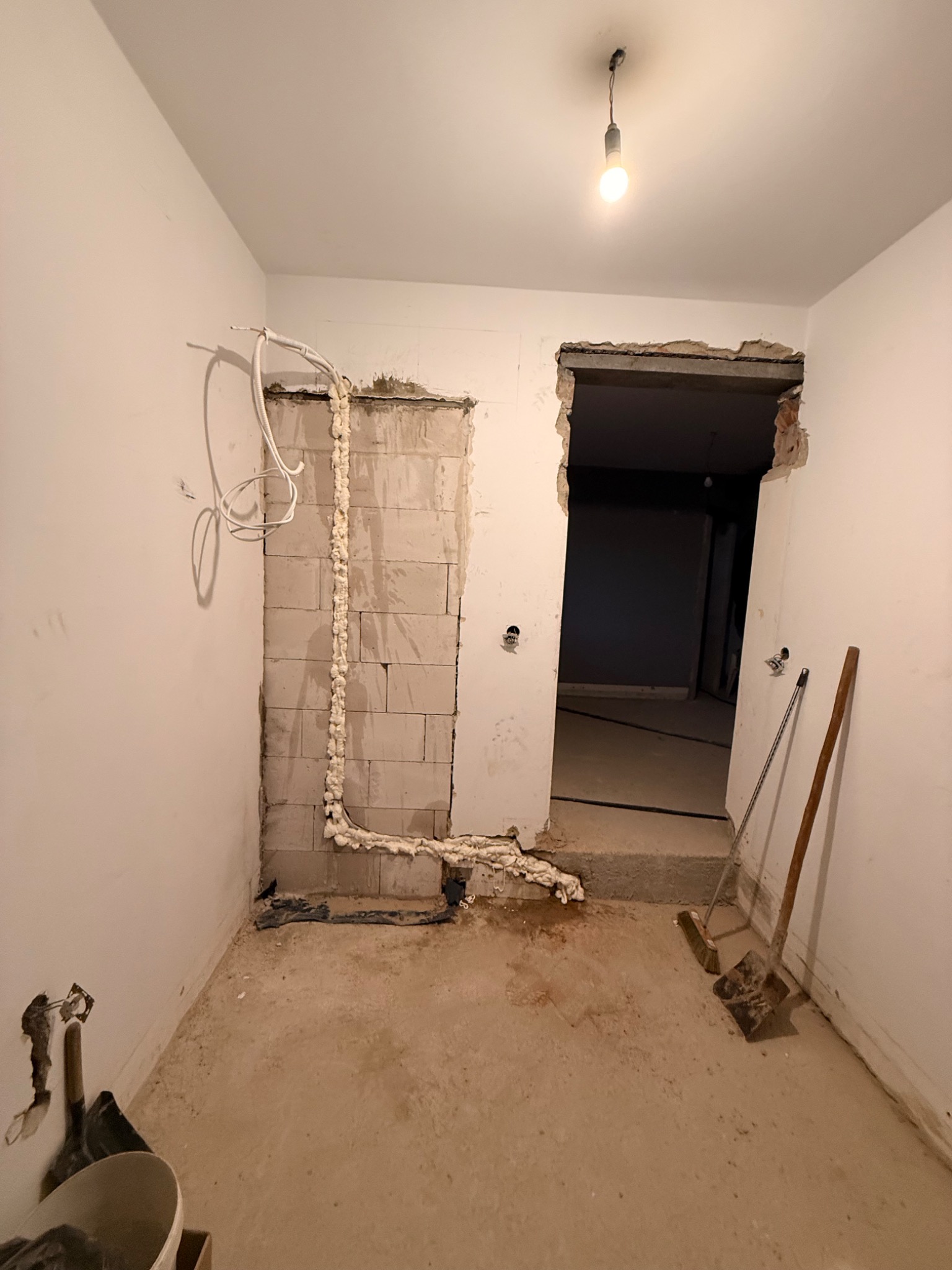 Wnętrze w trakcie remontu: instalacja przewodów zabezpieczonych pianką montażową na ścianie z pustaków, widoczne narzędzia i prowizoryczne oświetlenie.