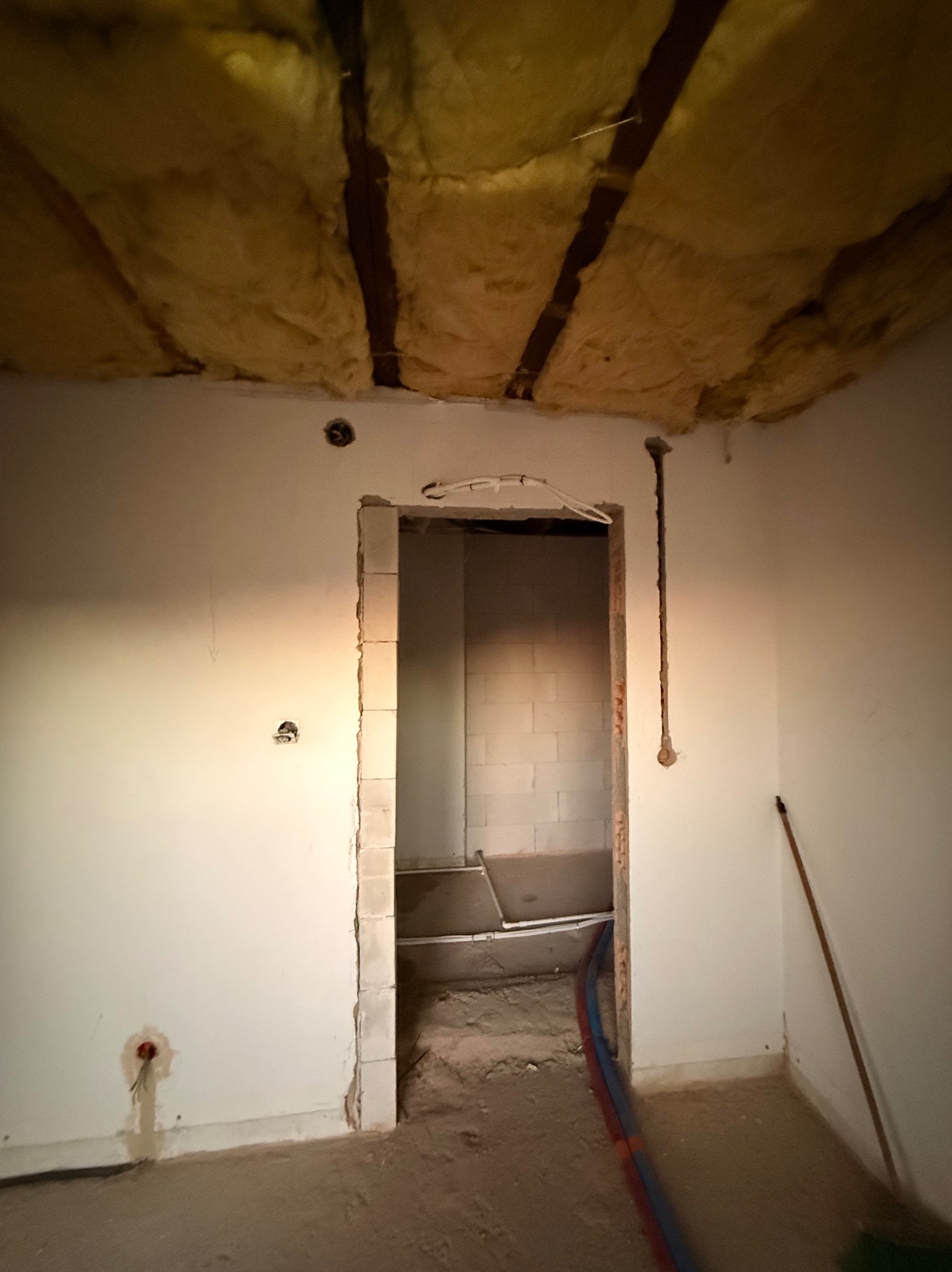 Wnętrze w trakcie prac instalacyjnych: ocieplony strop, bruzdy w ścianach pod instalacje, widoczne rury. Surowy stan, przygotowanie do dalszych prac wykończeniowych.