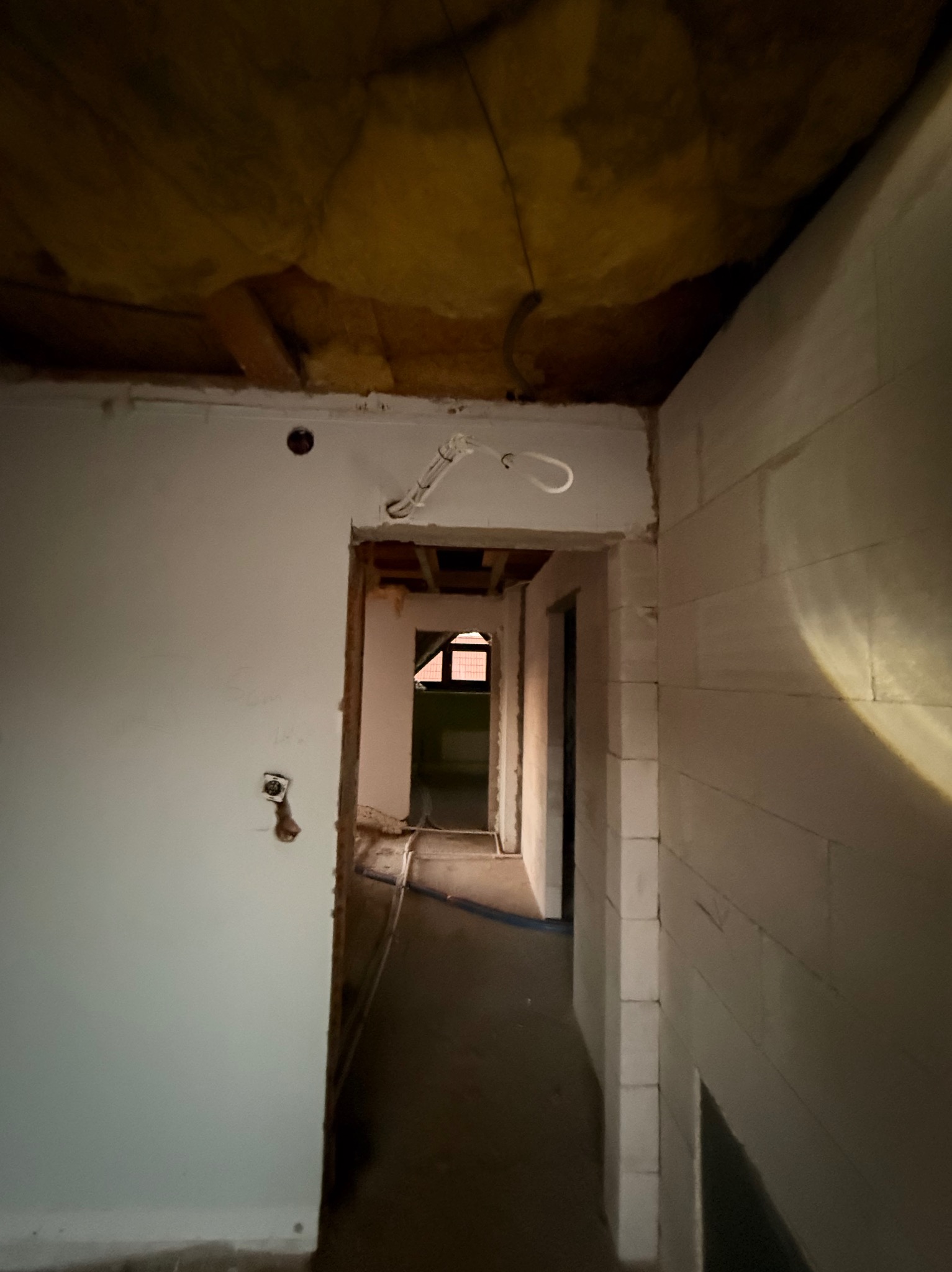 Wnętrze w trakcie prac instalacyjnych: widoczne przewody elektryczne wystające ze ściany, surowy stan wykończenia, ściany z białych bloczków.