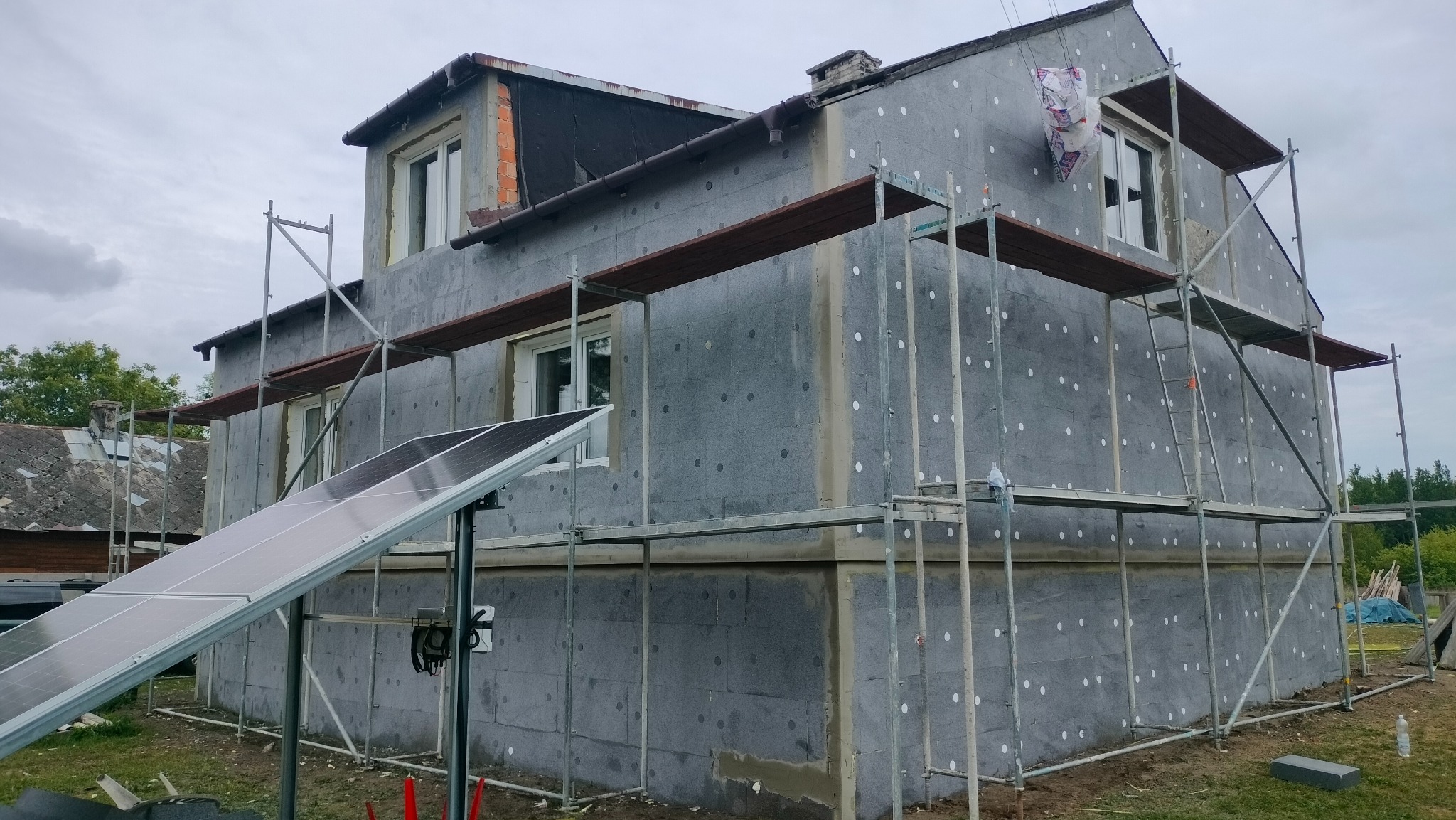 Dom w trakcie termomodernizacji z widocznymi rusztowaniami i zamontowanymi panelami słonecznymi na pierwszym planie.