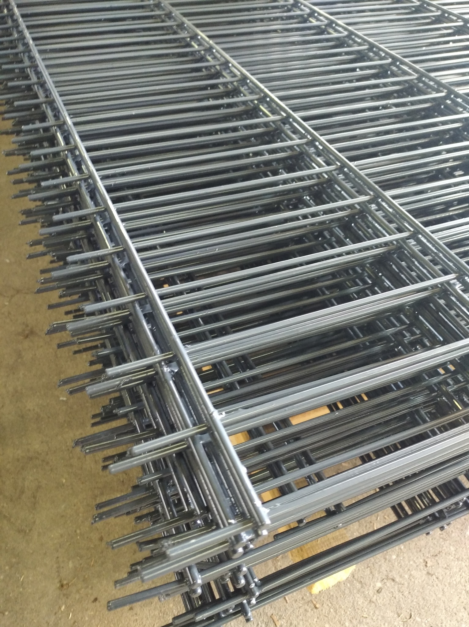 Stos paneli 2D z drutu stalowego, widoczne spawy i drobne niedoskonałości powłoki, leżące na palecie. Widok z góry pod kątem.