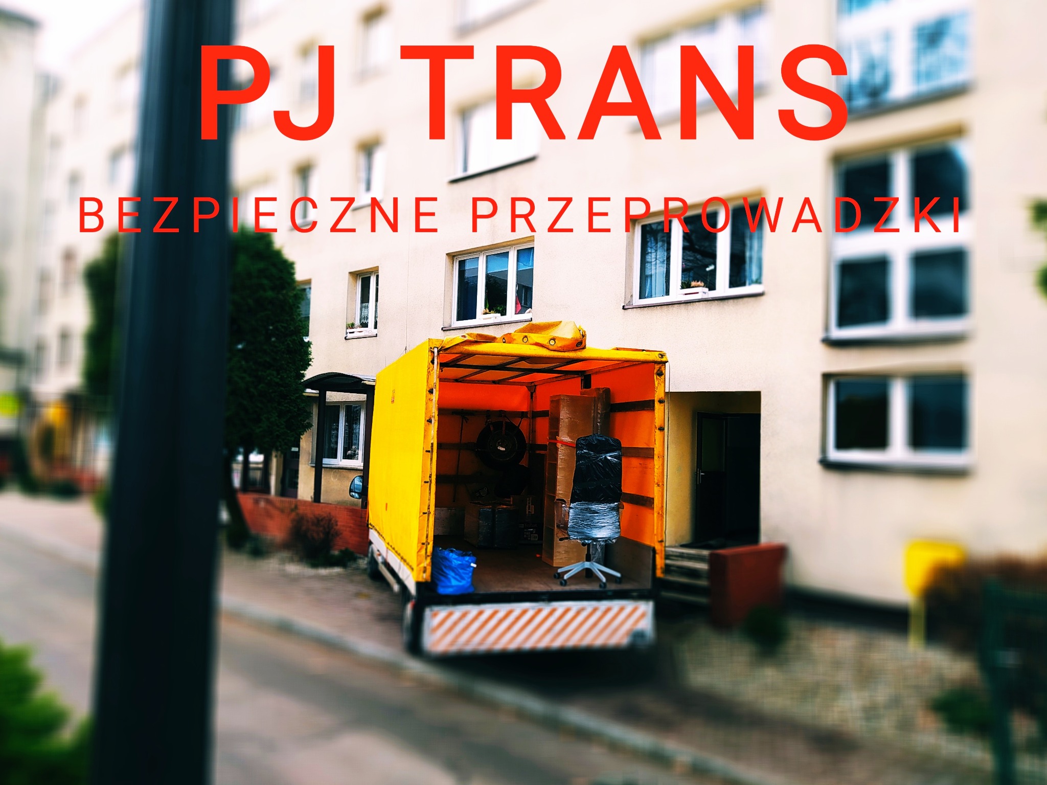 Otwarta paka żółtego samochodu dostawczego z napisem 'PJ TRANS BEZPIECZNE PRZEPROWADZKI' w tle budynku mieszkalnego, wewnątrz kartony i krzesło biurowe owinięte folią.