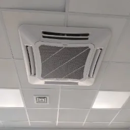 Kasetonowa jednostka wewnętrzna na suficie podwieszanym z widocznymi kratkami wentylacyjnymi i oświetleniem LED.