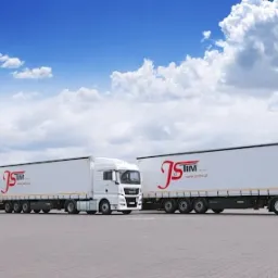Trzy białe ciężarówki z naczepami ustawione w rzędzie na parkingu, każda z logo firmy JS TIM, na tle błękitnego nieba z chmurami.