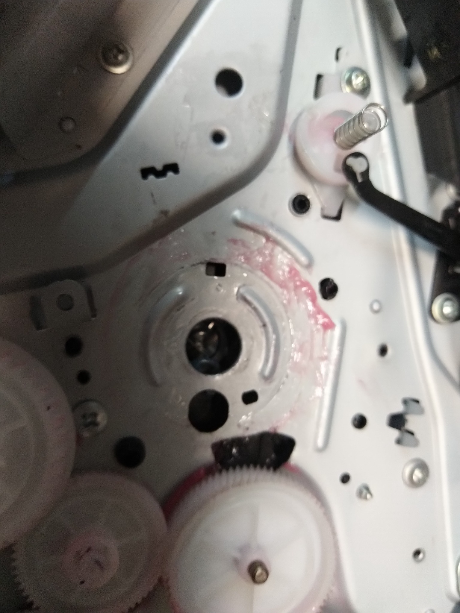 Wnętrze mechanizmu kserokopiarki z widocznymi plastikowymi zębatkami, smarem w kolorze różowym i elementami metalowymi podczas konserwacji.