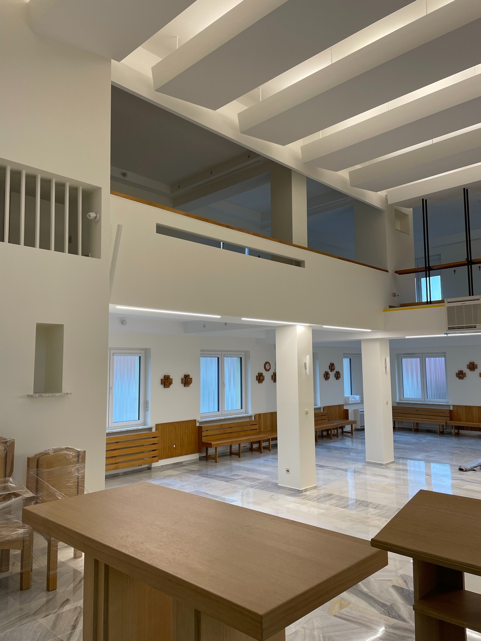 Jasne, przestronne wnętrze po remoncie w Łętowni, z marmurową posadzką i białymi ścianami. Widoczne drewniane ławki, kolumny i podwieszany sufit z oświetleniem liniowym.