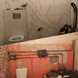 Usługi remontowo wykończeniowe Piotr Sobieraj - Dzielone ujęcie łazienki w trakcie metamorfozy: górna część pokazuje nową toaletę z biało-marmurowymi płytkami, dolna część ukazuje starą instalację z odsłoniętą rurami i resztkami tapety.