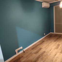 Usługi remontowo wykończeniowe Piotr Sobieraj - Pomieszczenie po odświeżeniu: turkusowa ściana, drewnopodobna podłoga, biała listwa przypodłogowa, klimatyzator na ścianie, widoczne gniazdka elektryczne.