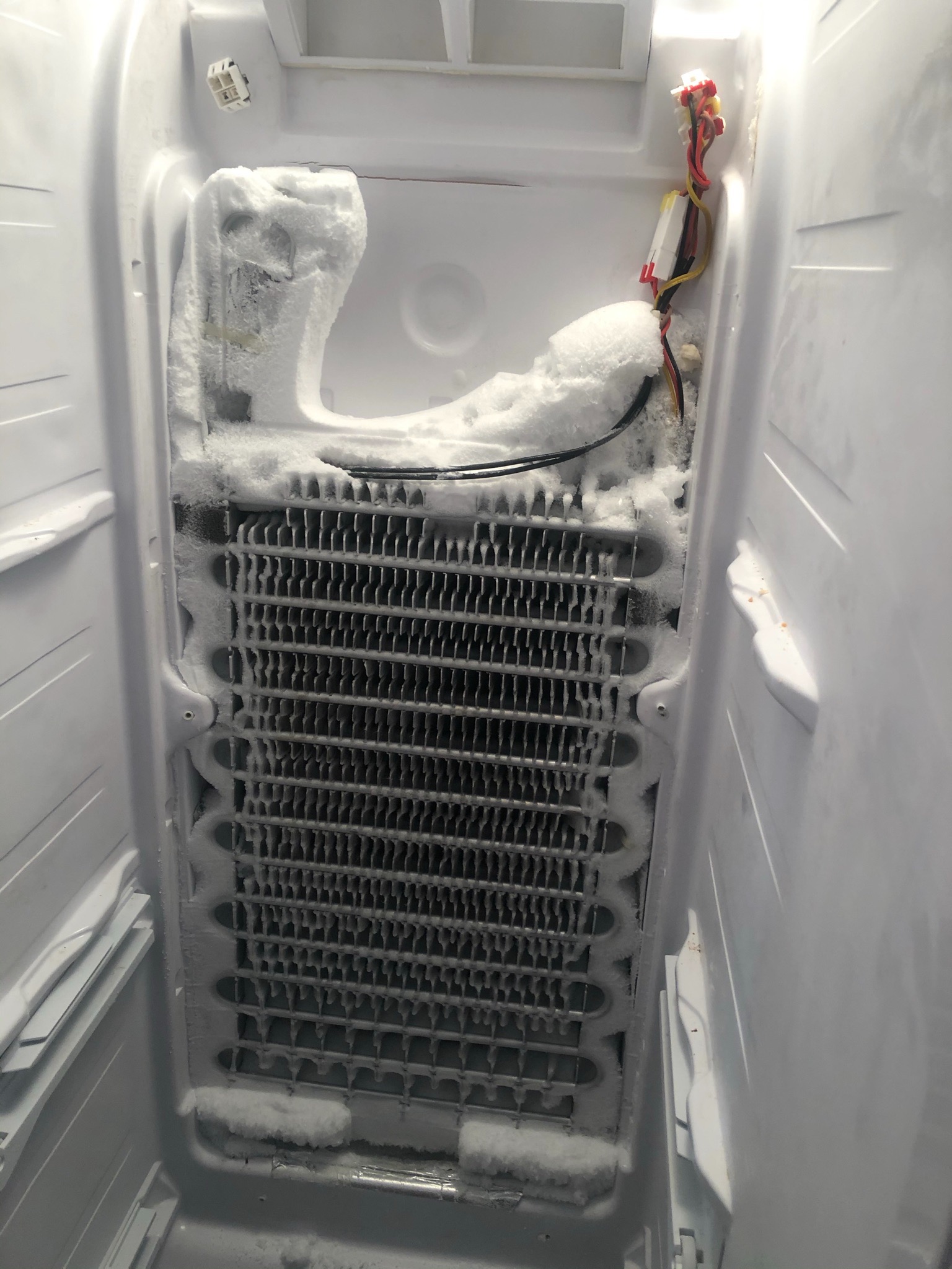 Wnętrze zamrażarki z silnym oblodzeniem na radiatorze i elementach konstrukcyjnych, widoczne przewody elektryczne.