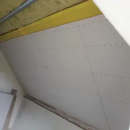 Ocieplenie poddasza z widoczną wełną mineralną i zamontowanymi płytami kartonowo-gipsowymi, widoczne ślady po wkrętach na płytach, perspektywa z dołu.