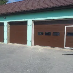 Trzy brązowe bramy segmentowe w budynku o turkusowych ścianach i brązowym dachu, jedna z bram z dodatkowymi oknami i drzwiami wejściowymi.