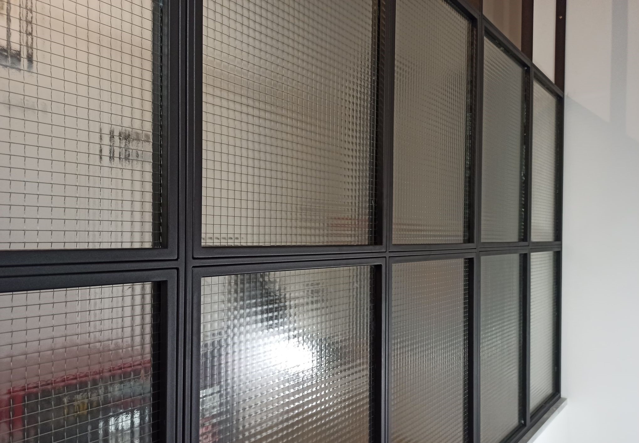 Szklana ściana działowa z metalową ramą w loftowym stylu, widok z boku, z delikatną fakturą szkła i odbiciami światła.