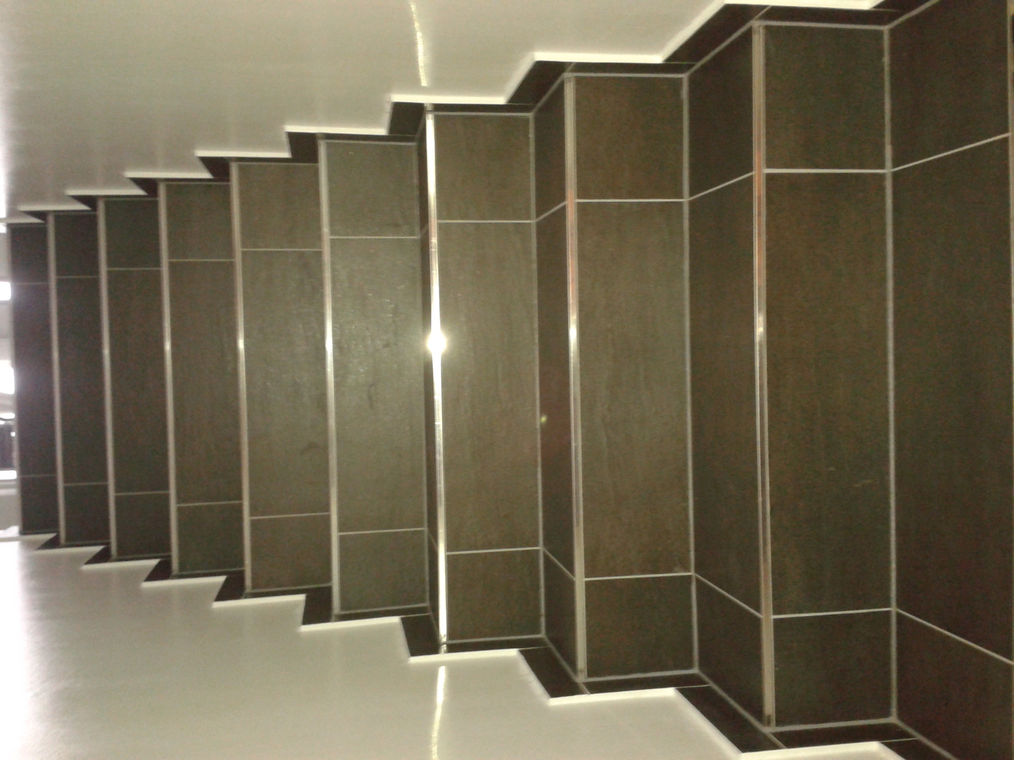 Wykończone schody wewnątrz budynku, obłożone ciemnobrązowymi płytkami z jasnymi fugami, widoczne z góry w perspektywie.